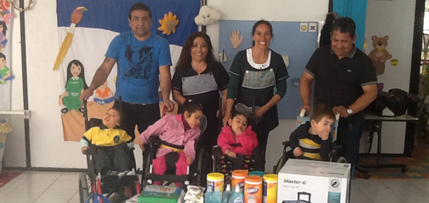 Group of adults and children with disabilities smiling, with various donations on a table in front.